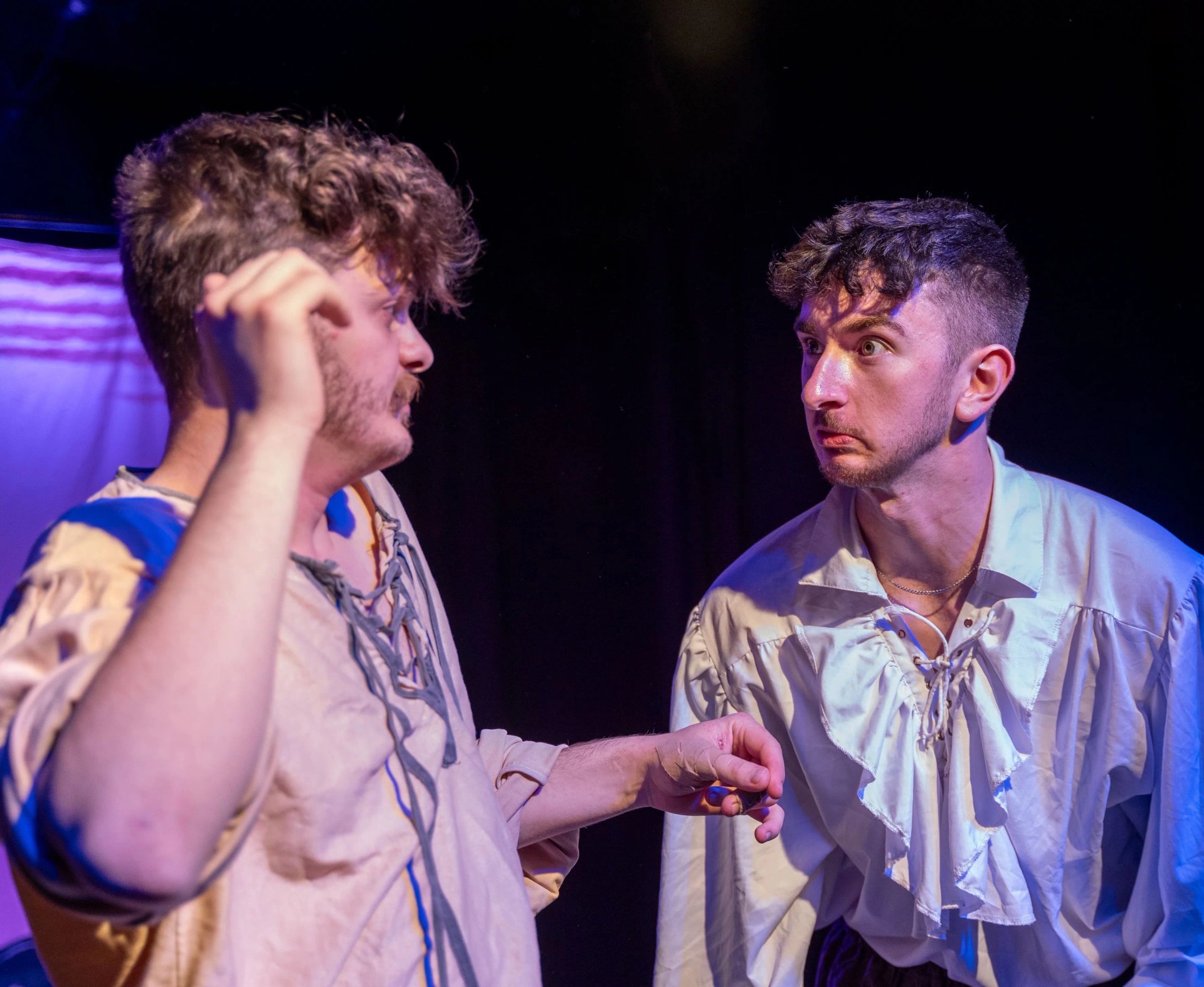 Two men look at each other in exasperation. They are wearing white frilly shirts.