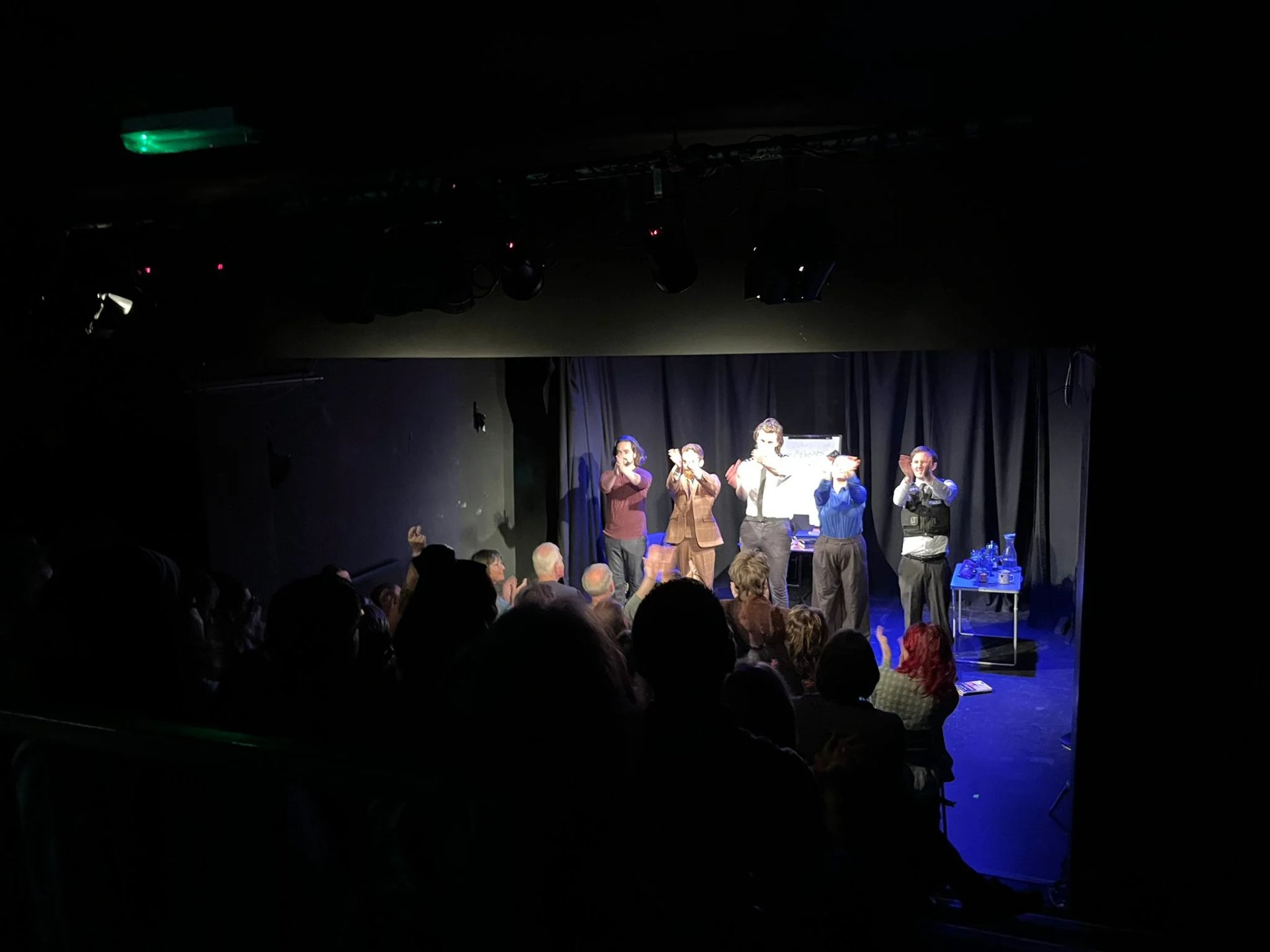 A group photo of 5 cast members clapping towards the audience. 