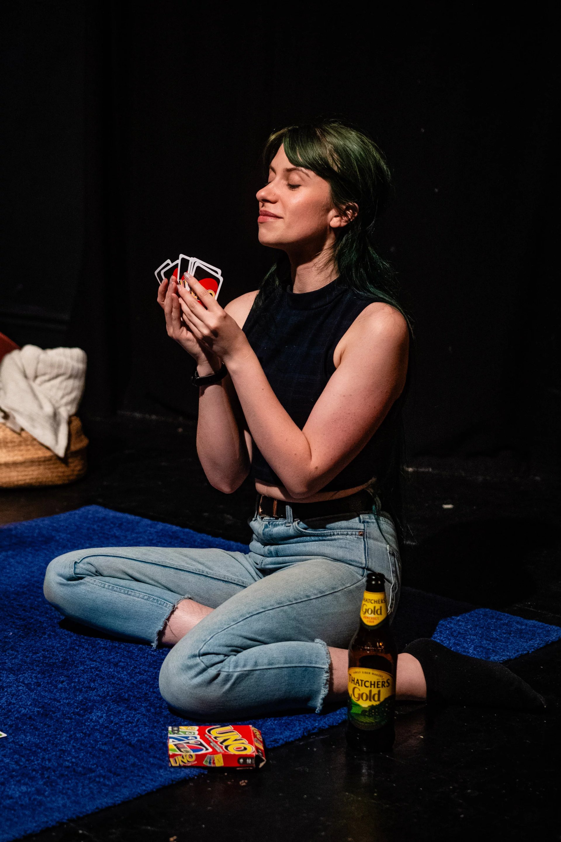 Billie-Jo as Mercy in love you, bye. She is sat on the floor with Uno cards in her hand. She is looking smug.