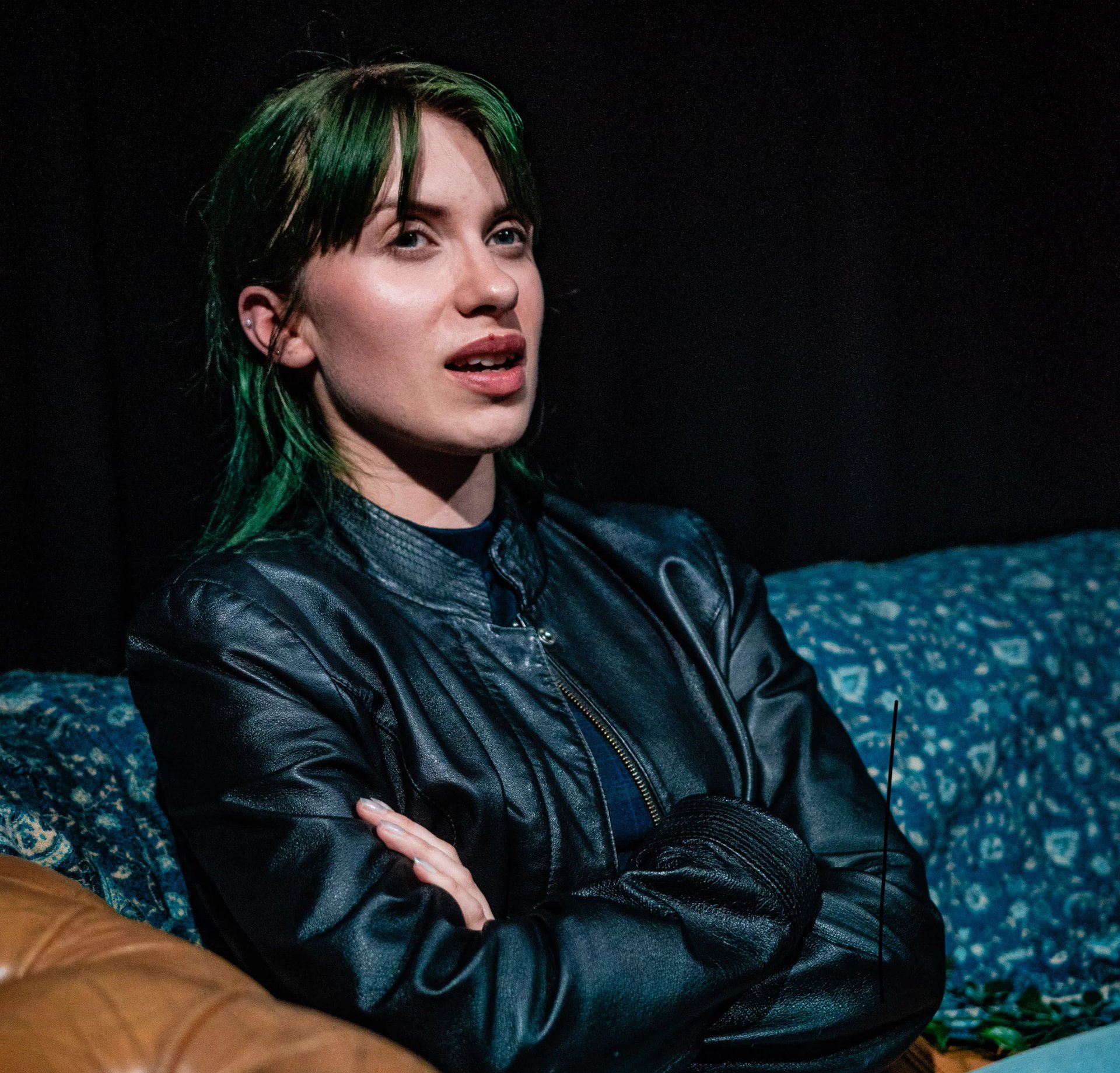 Billie-Jo as Mercy in Love you, bye. She is sat on a sofa wearing a black leather jacket.