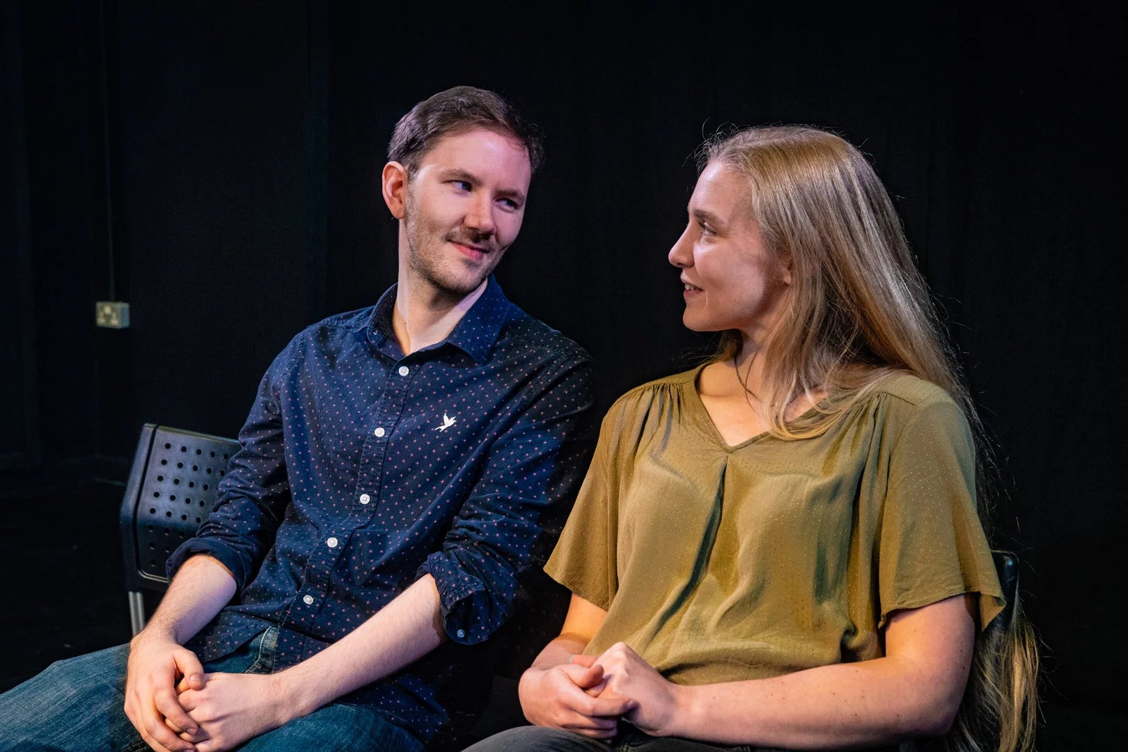 Two actors sit next to each other, they look happy and comfortable together.