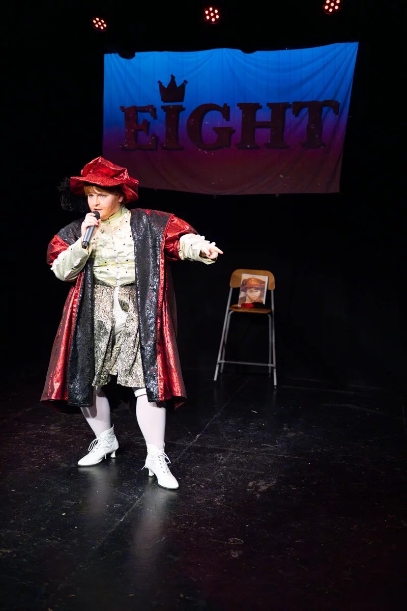 Henry the eighth is mid song. The projected image behind them says eight in glittering letters.