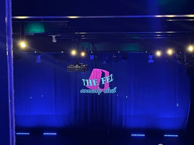A stage photo with the Fez Comedy logo projected onto the curtains.