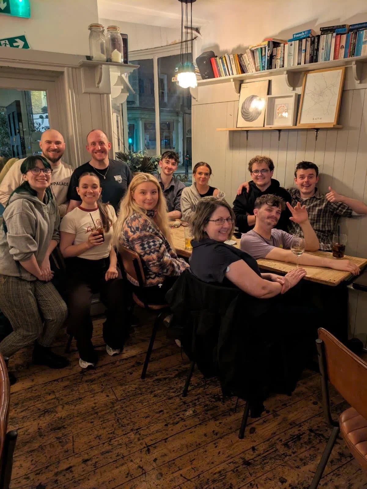 A group photo in a pub with people sat and stood around a table smiling. They are the cast and crew of Five Weeks