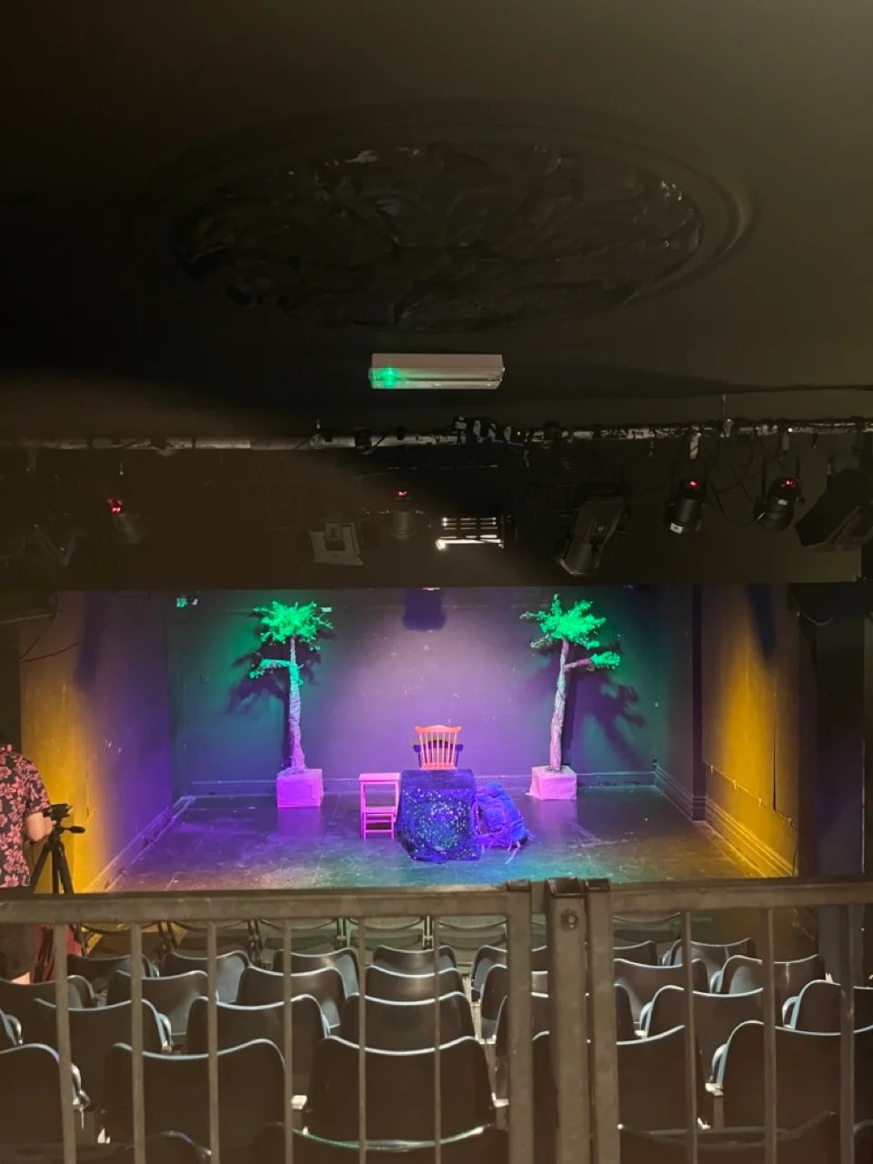 A stage photo from the top of the audience. Nigel Planer stands onstage in a spot light, purple lighting covers the stage