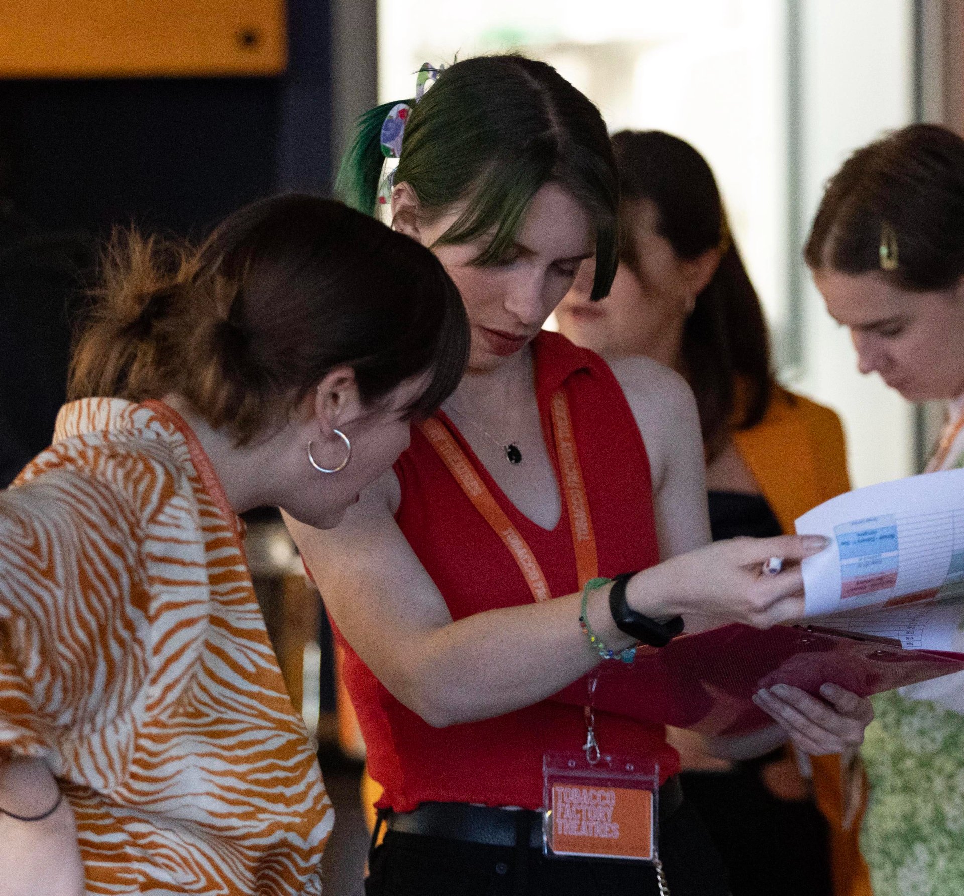 Billie-Jo Rainbird as a producer at Tobacco Factory Theatres. She and another person is looking at notes on a clipboard. She is wearing a red top and an orange lanyard.